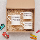 A perfect superhero gift set with one “Superhero in Disguise” mug and two “Superhero in Training” mugs, nestled in an open kraft gift box with shredded paper