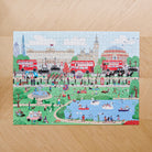 Completed Dog Walkers of London jigsaw puzzle on wooden surface — 1000 piece illustrated London scene with Buckingham Palace, Big Ben and Royal Albert Hall, dog lover gift by Sweet William Designs