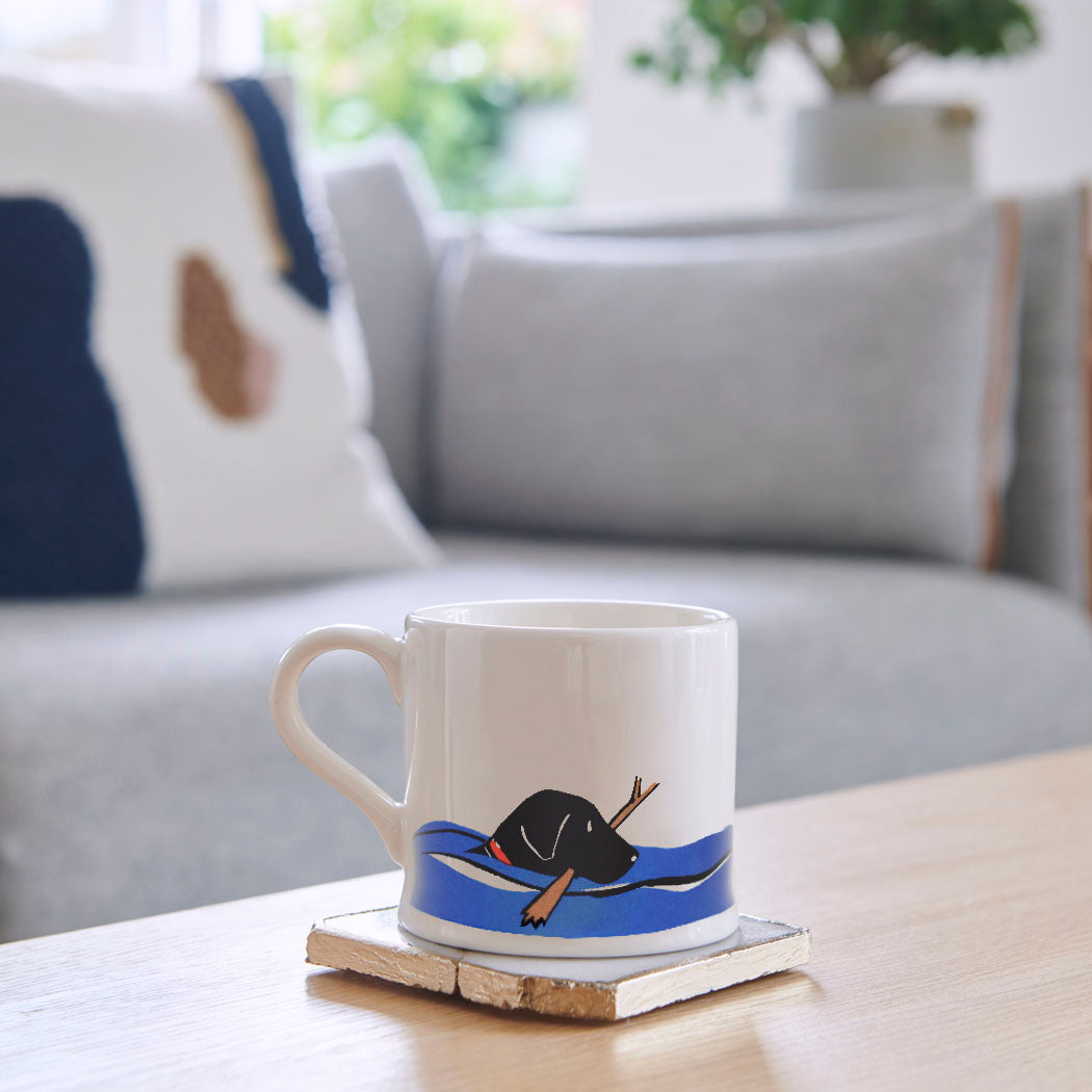 Swimming Black Labrador mug on a coffee table — ceramic dog lover gift by Sweet William Designs
