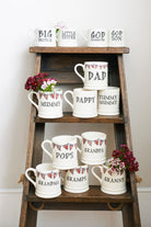 Group of ceramic Grandparent mugs displayed on wooden ladders, showing different family-name choices, each decorated with hand-drawn Union Jack bunting