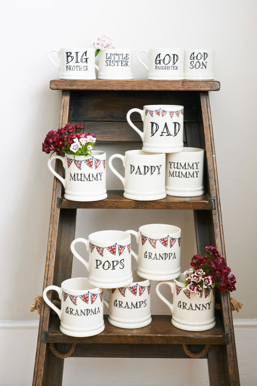 Group of ceramic Grandparent mugs displayed on wooden ladders, showing different family-name choices, each decorated with hand-drawn Union Jack bunting