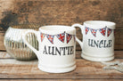 Ceramic Auntie and Uncle mugs from Sweet William Designs with Union Jack bunting, styled with a silver candle and star decoration on a rustic wooden surface