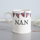 Ceramic Nan mug with hand-drawn Union Jack bunting, styled beside delicate white flowers, a thoughtful gift for a much-loved grandparent