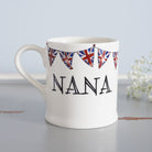 Ceramic Nana mug with hand-drawn Union Jack bunting, styled beside delicate white flowers, a thoughtful gift for a much-loved grandparent