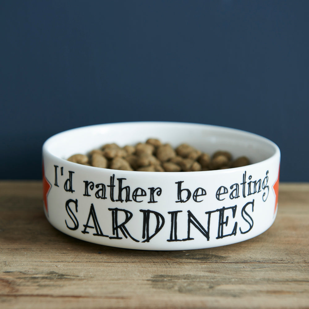 White porcelain cat bowl with “I’d Rather Be Eating Sardines” slogan and red star accents on a wooden table