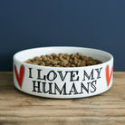 'I Love My Humans' white porcelain cat bowl with red hearts and hand-drawn black lettering, shown on a rustic wooden table