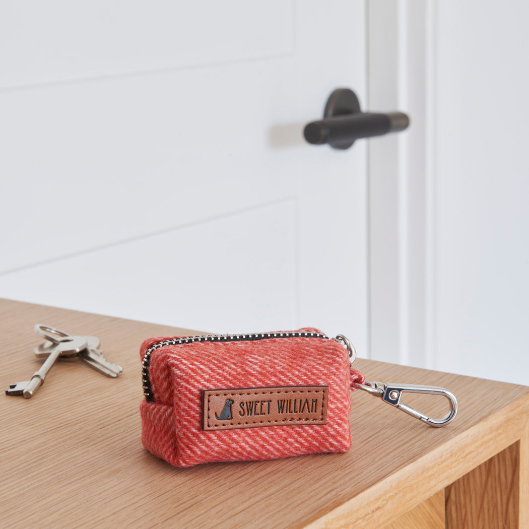 Orange tweed dog poo bag holder with a zip, clip and Sweet William label, resting on a wooden table