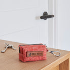 Orange tweed dog poo bag holder with a zip, clip and Sweet William label, resting on a wooden table