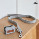 Grey tweed dog poo bag holder with a zip, clip and Sweet William label beside its matching dog lead on a wooden table