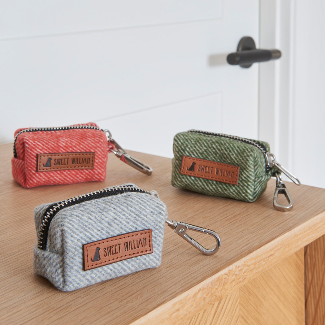 The full Sweet William tweed poo bag holder colour range in grey, green and orange, lined up on a wooden table
