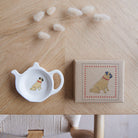 White teapot-shaped Pug teabag dish beside its kraft gift box, both featuring a fawn Pug illustration with red collar