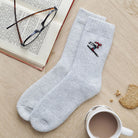 Embroidered skier wool socks laid flat beside a book, glasses and a cup of tea — cosy ski lover gift by Sweet William Designs