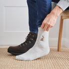 Man pulling on hare wool socks with walking boots indoors — unisex embroidered wool blend socks by Sweet William Designs
