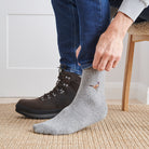Man pulling on pheasant wool socks with walking boots indoors — unisex embroidered wool blend socks by Sweet William Designs
