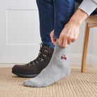 Man pulling on embroidered red tractor wool socks with walking boots indoors — unisex wool blend socks by Sweet William Designs
