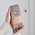 Sheep wool socks held in hands with Sweet William Designs branded band — soft wool blend sheep lover gift
