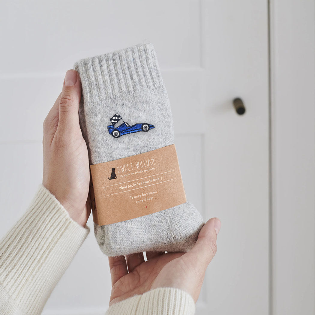 Embroidered blue racing car wool socks held in hands with Sweet William Designs branded band — a thoughtful gift for racing fans