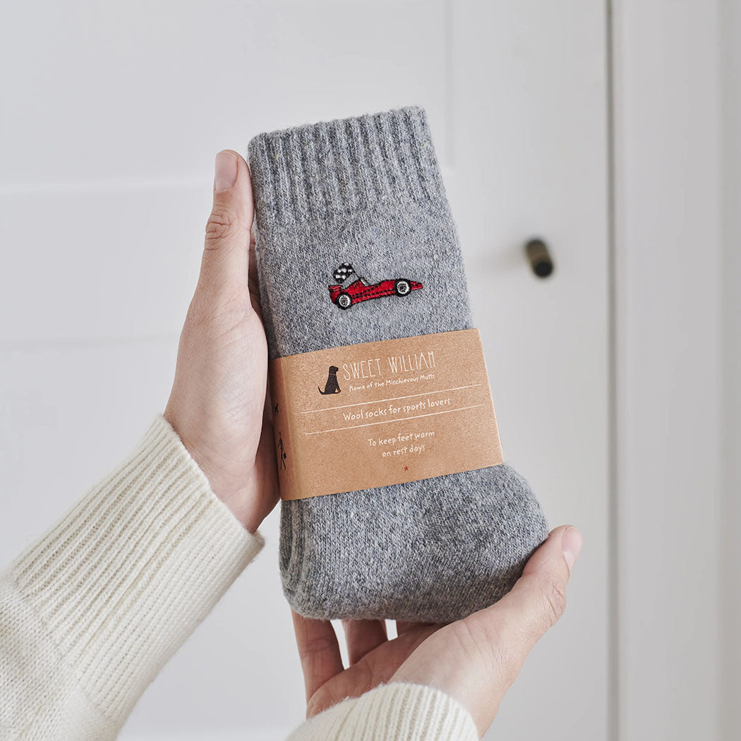 Embroidered red racing car wool socks held in hands with Sweet William Designs branded band — a thoughtful gift for racing fans