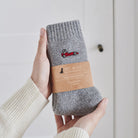 Embroidered red racing car wool socks held in hands with Sweet William Designs branded band — a thoughtful gift for racing fans