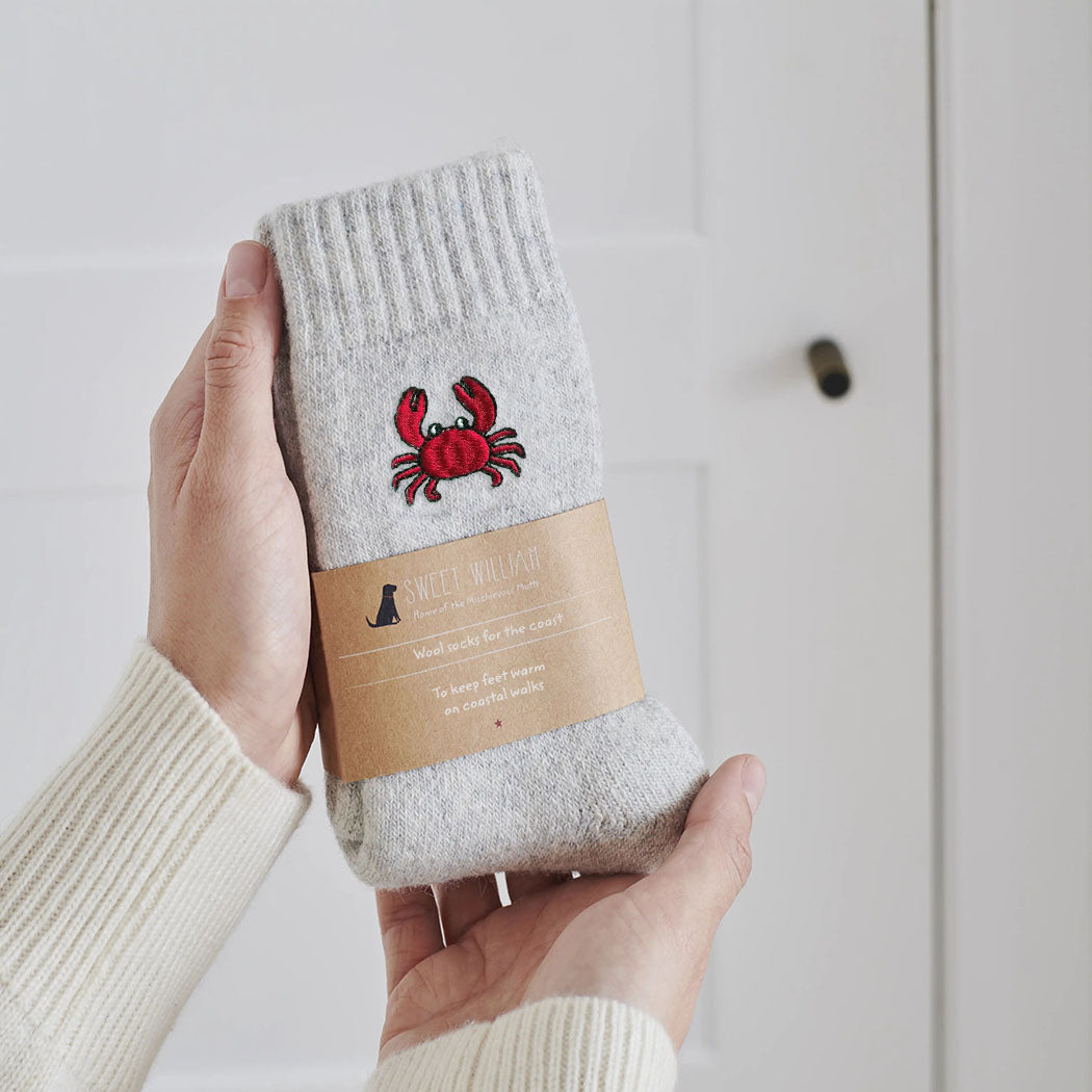 Crab wool socks held in hands with Sweet William Designs packaging band — embroidered coastal gift for beach lovers