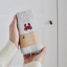 Crab wool socks held in hands with Sweet William Designs packaging band — embroidered coastal gift for beach lovers