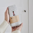 Lighthouse wool socks held in hands with Sweet William Designs packaging band — embroidered coastal gift for seaside lovers

