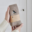 Puffin wool socks held in hands with Sweet William Designs packaging band — embroidered coastal gift for seaside lovers