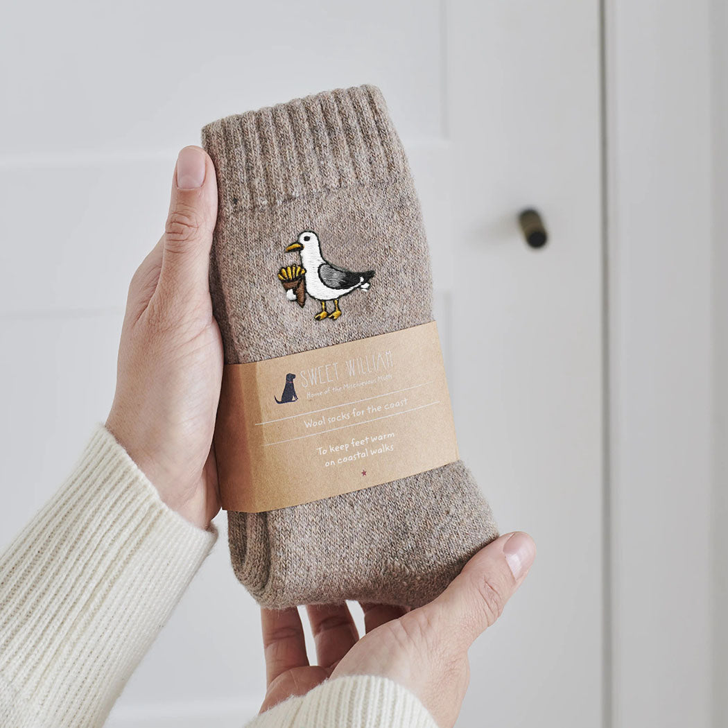 Seagull wool socks held in hands with Sweet William Designs packaging band — embroidered coastal gift for seaside lovers