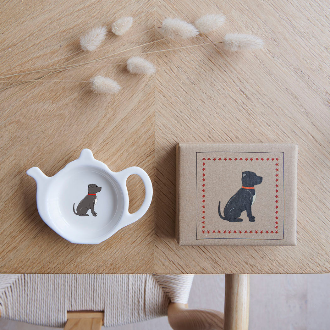 White teapot-shaped Staffie teabag dish beside its kraft gift box, both featuring a grey Staffordshire Bull Terrier illustration with a white chest and red collar