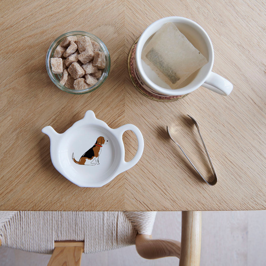 White teapot-shaped Beagle teabag dish with a Beagle illustration and red collar, beside a mug, sugar cubes and sugar tongs