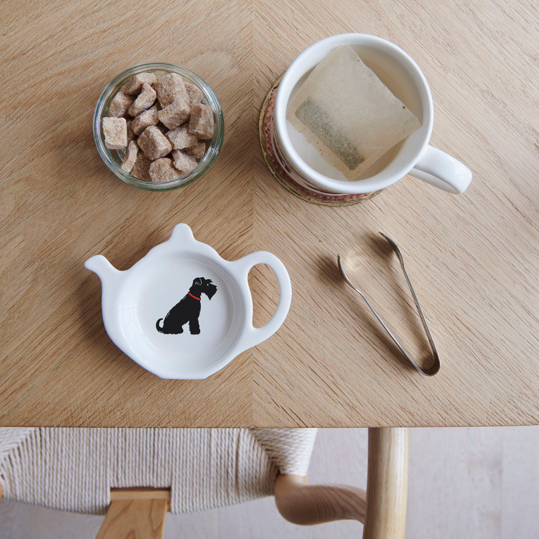 White teapot-shaped Black Schnauzer teabag dish with a black dog illustration and red collar, beside a mug, sugar cubes and sugar tongs