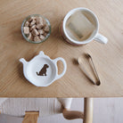White teapot-shaped Chocolate Cockapoo / Labradoodle teabag dish with a brown dog illustration and red collar, beside a mug, sugar cubes and sugar tongs