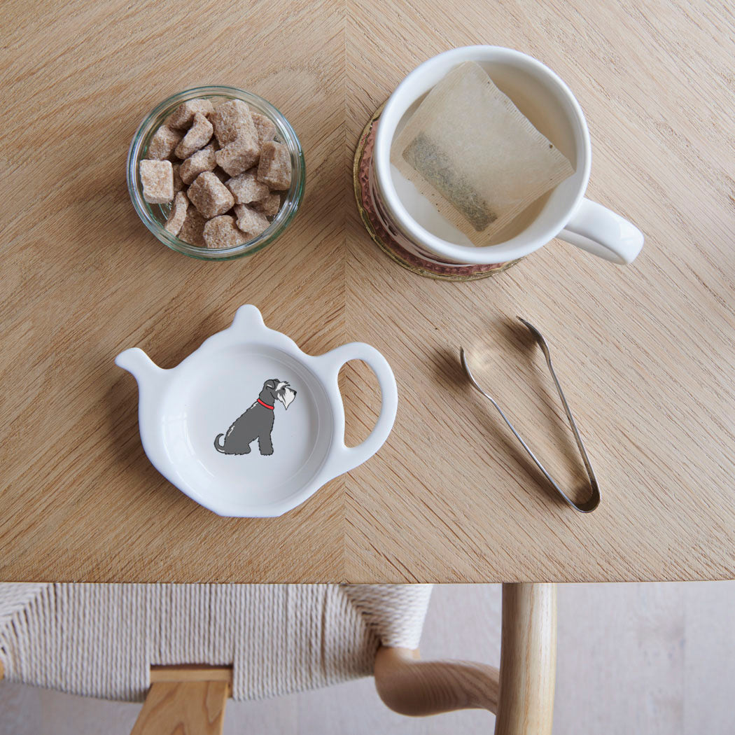 White teapot-shaped Salt & Pepper Schnauzer teabag dish with a grey dog illustration, white beard and red collar, beside a mug, sugar cubes and sugar tongs