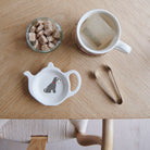 White teapot-shaped Salt & Pepper Schnauzer teabag dish with a grey dog illustration, white beard and red collar, beside a mug, sugar cubes and sugar tongs