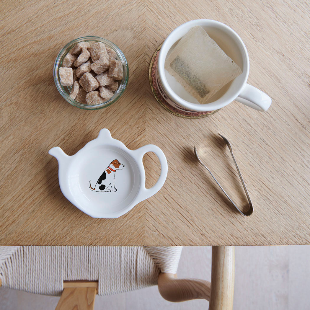 White teapot-shaped Jack Russell teabag dish with a tricolour dog illustration and red collar, beside a mug, sugar cubes and sugar tongs