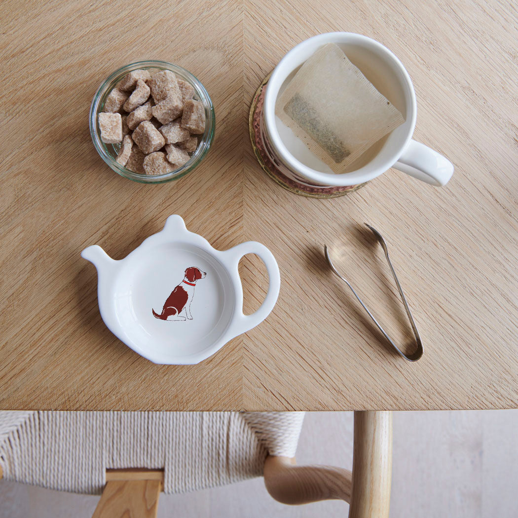 White teapot-shaped Liver & White Springer Spaniel teabag dish with a dog illustration and red collar, beside a mug, sugar cubes and sugar tongs