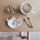 White teapot-shaped Vizsla teabag dish with a golden-brown dog illustration and red collar, beside a mug, sugar cubes and sugar tongs