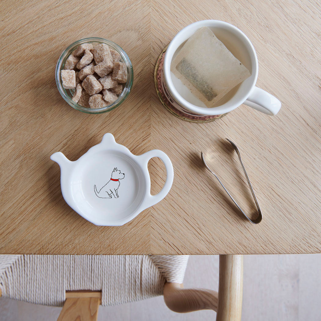 White teapot-shaped Westie teabag dish with a white dog illustration and red collar, beside a mug, sugar cubes and sugar tongs