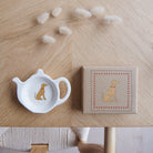White teapot-shaped Vizsla teabag dish beside its kraft gift box, both featuring a golden-brown Vizsla illustration with a red collar