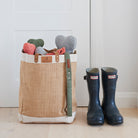 Grey, green and orange tweed dog bone toys peeking out of a Sweet William jute bag beside a pair of Hunter wellies