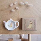 White teapot-shaped Yellow Labrador teabag dish beside its kraft gift box, both featuring a Yellow Lab illustration with a red collar