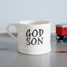 Ceramic “God Son” mug photographed beside a red toy train, a thoughtful gift for a godson