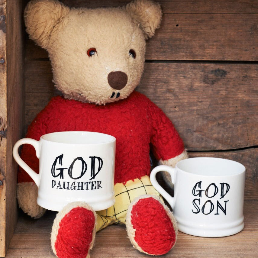 Ceramic “God Daughter” and “God Son” mugs styled with a teddy bear on a rustic wooden shelf, a lovely godchild gift