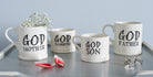 Ceramic Godmother, Godfather, God Daughter and God Son mugs displayed together with flower petals and silver cufflinks, showing full collection by Sweet William Designs