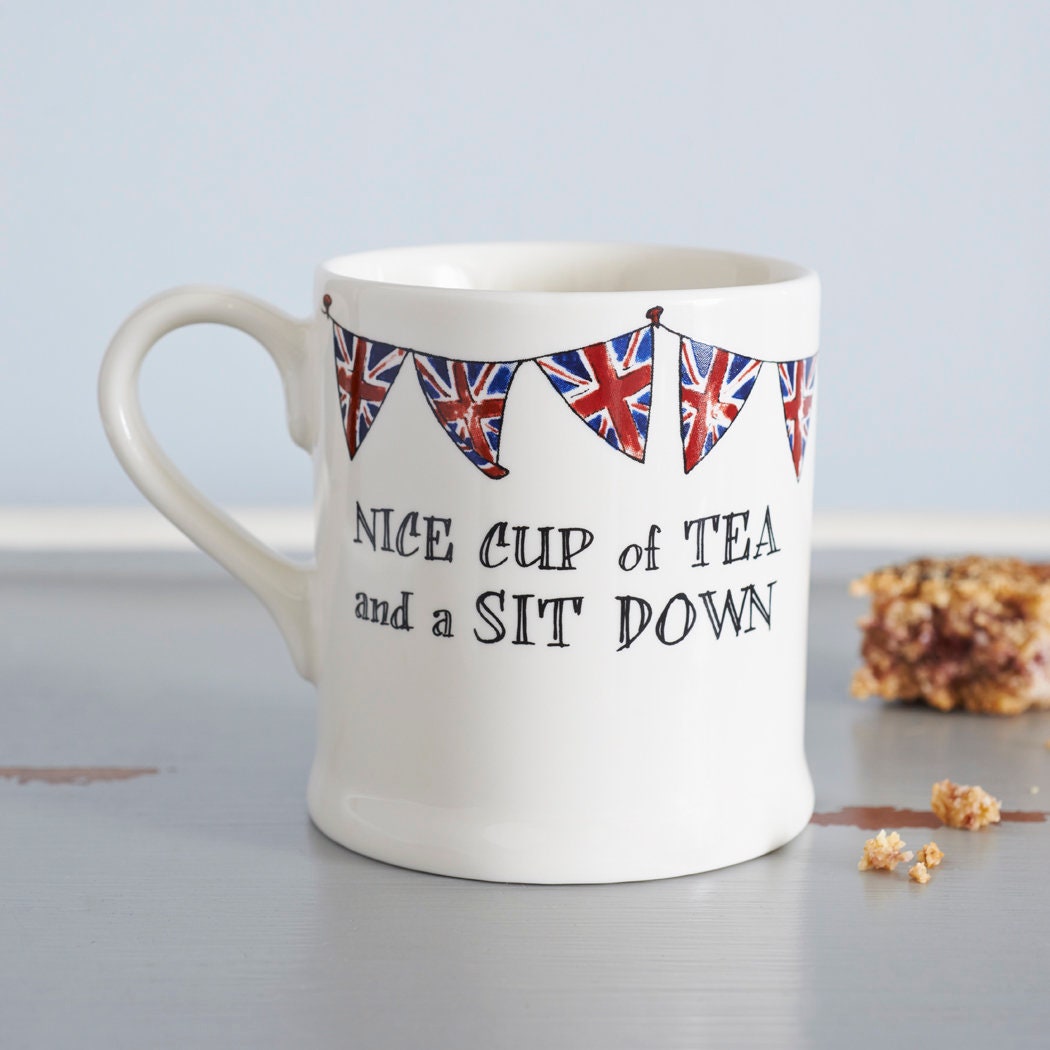 Ceramic mug with Union Jack bunting and a “Nice cup of tea and a sit down” message beside a biscuit, a perfect gift for tea lovers