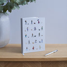 Dog Walker's Notebook standing upright on wooden surface — pale grey illustrated hardback A5 notebook, perfect gift for dog walkers by Sweet William Designs
