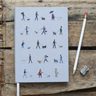 Close-up of Dog Walker's Notebook cover — illustrated dog walkers and dogs on pale grey hardback, A5 lined notebook, dog lover stationery gift