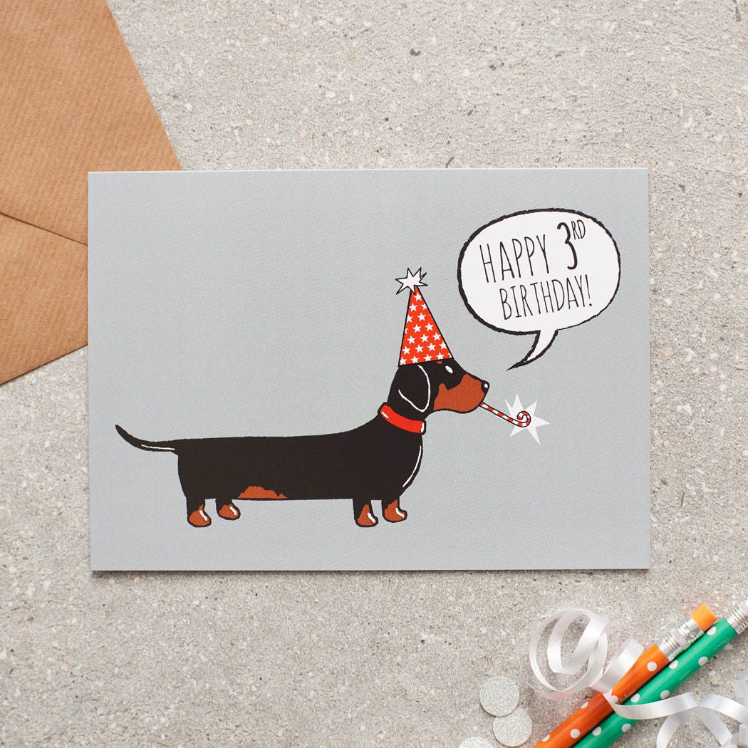 Dachshund 3rd birthday card featuring a black and tan sausage dog in a red party hat with a “Happy 3rd Birthday!” message, designed by Sweet William Designs