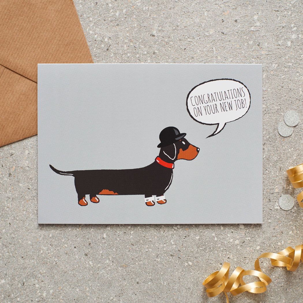 Dachshund new job congratulations card by Sweet William Designs, featuring an illustrated black and tan Dachshund wearing a bowler hat and red collar, with “Congratulations on your new job!” message and kraft envelope