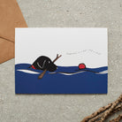 Swimming Black Labrador card featuring a water-loving Lab chasing a ball while holding a stick, with the words “Happiness is a ball and a stick” by Sweet William Designs